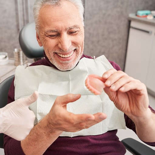 Man smiling holding new dentures with dentist giving thumbs up