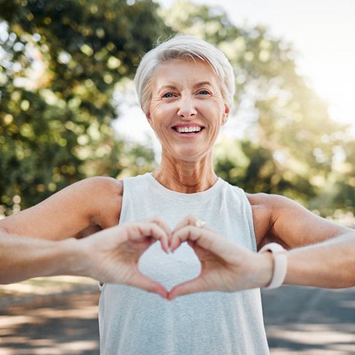 Lady smiles outdoors while making shape of heart with her hands