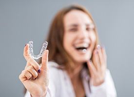 Laughing woman blurry in background holding Invisalign to foreground