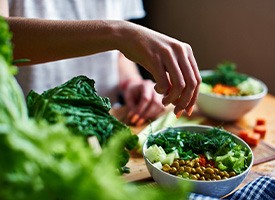 Hands at cutting board putting placing vegetables into salad bowls