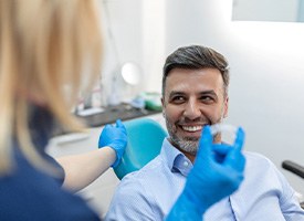 Man in dental chair smiling at dentist about to hand him Invisalign