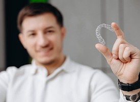 Man blurry in background holding Invisalign tray to foreground