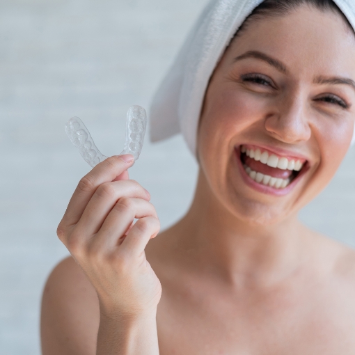 Smiling woman holding clear nightguard for bruxism