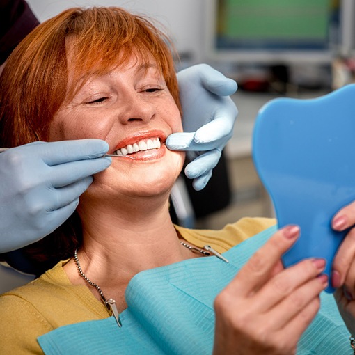 Woman with red hair smiling into mirror as dentist touches her teeth