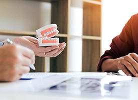 Dentist’s and patient’s hands at desk holding model teeth looking at x-rays