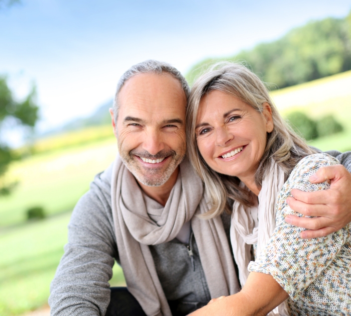 Older man and woman with healthy smiles thanks to tooth replacement with dental implants