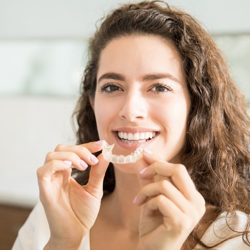 Smiling woman holding Invisalign clear braces tray