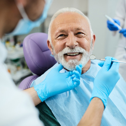 Man with white hair and beard smiling at dentist about to examine his teeth