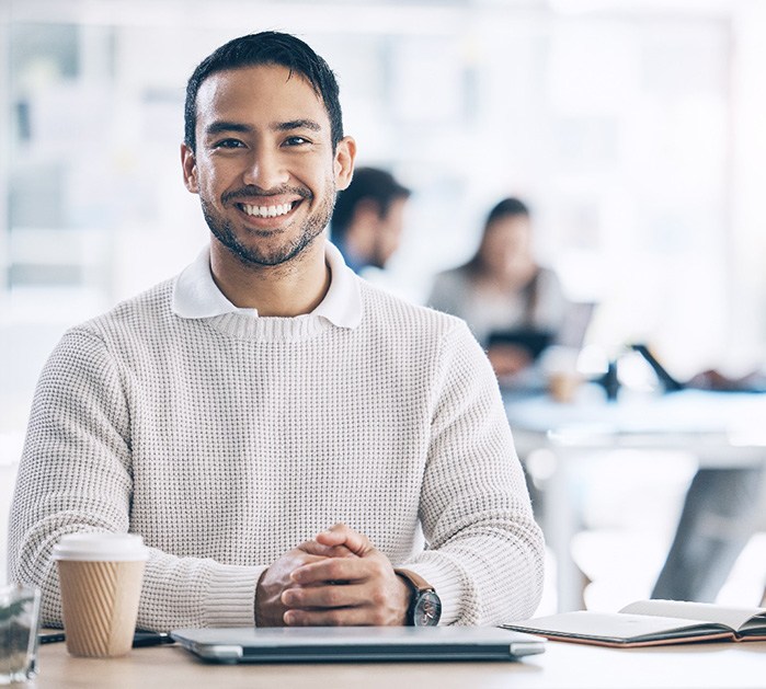 smiling man sitting at his office desk with a cup of coffee