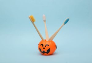 3 wooden toothbrushes in a plastic toy jack-o-lantern in front of a blue background