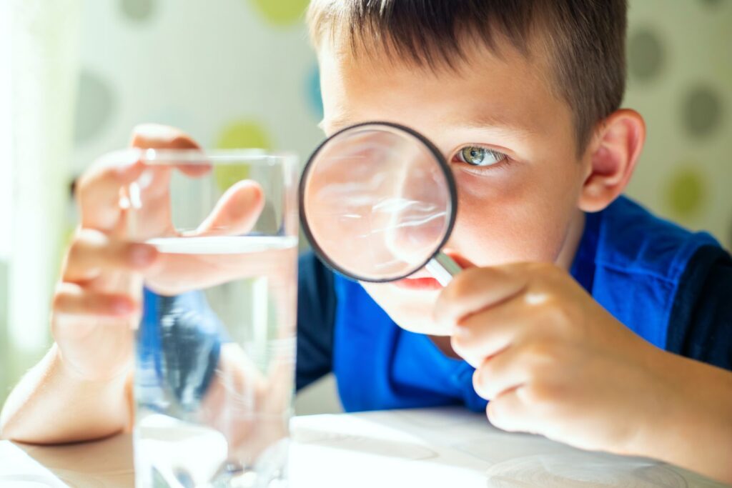 A little boy looking at a cup of water with a magnifying glass